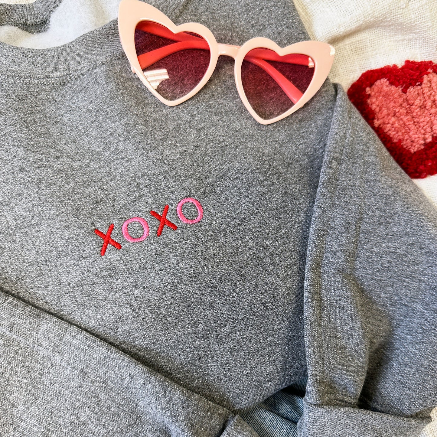 close up of a crewneck sweatshirt with a mini xoxo embroidered design in red and pink on the center chest