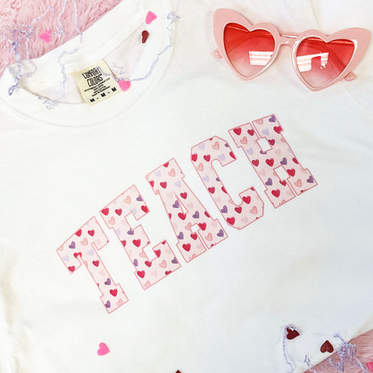 close  up of a TEACH printed design on a white t-shirt with a watercolor heart fill pattern