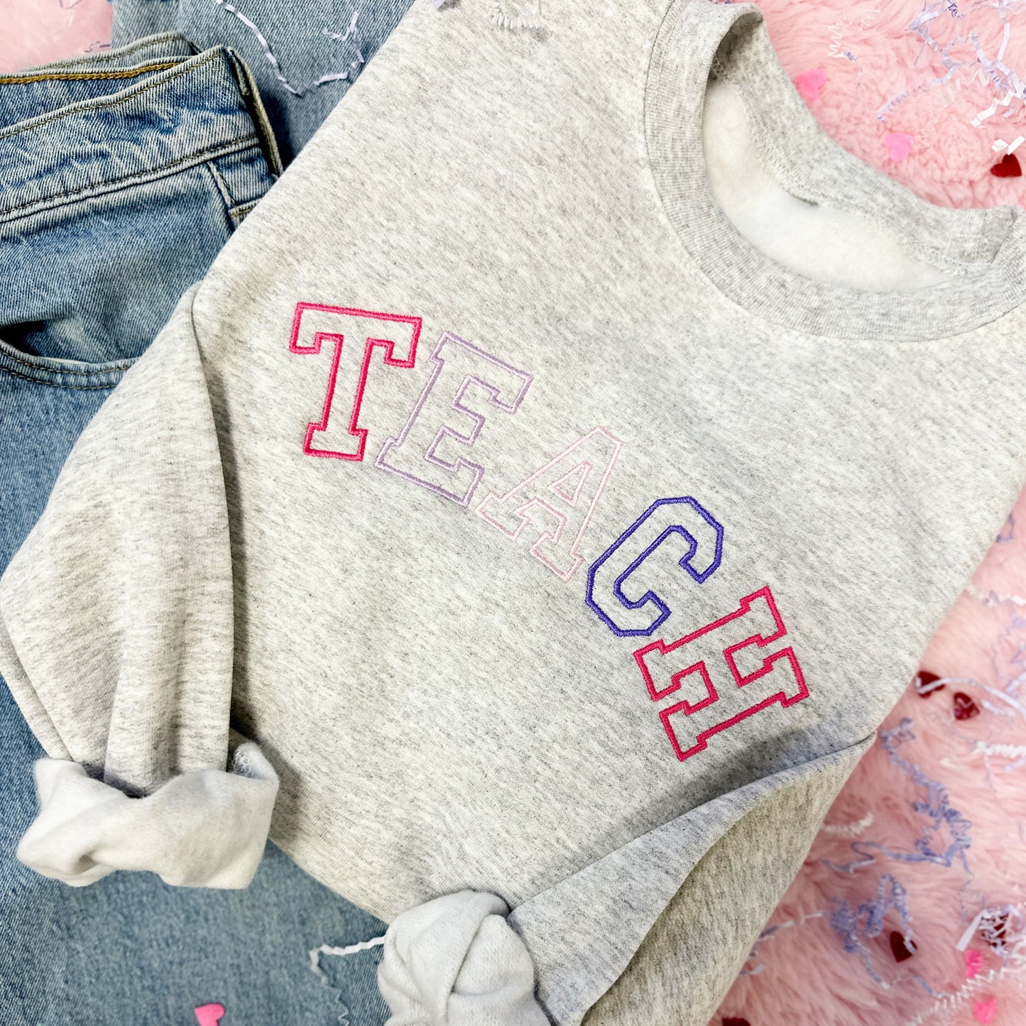ash gray sweatshirt with TEACH embroidered in pink and purple threads in an athletic block font across the chest