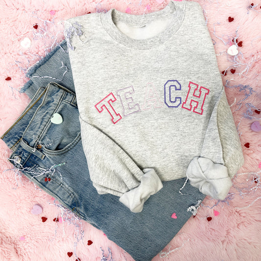 jeans paired with a light grey crewneck with TEACH embroidered across the chest in pink and purple thread