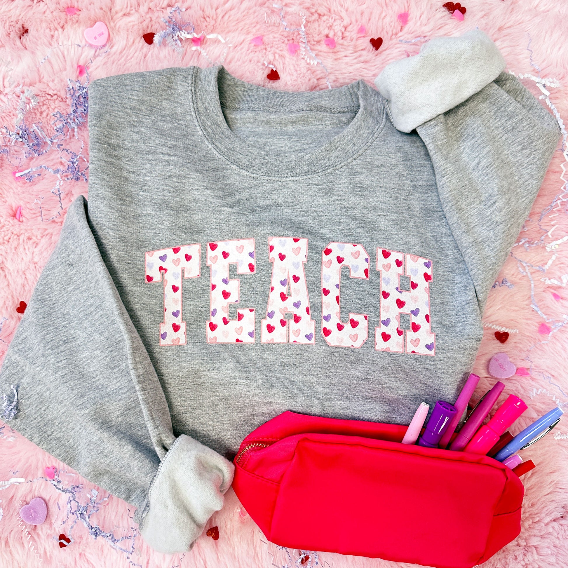 gray crewneck sweatshirt with TEACH printed across the chest with a watercolor heart patterned fill background
