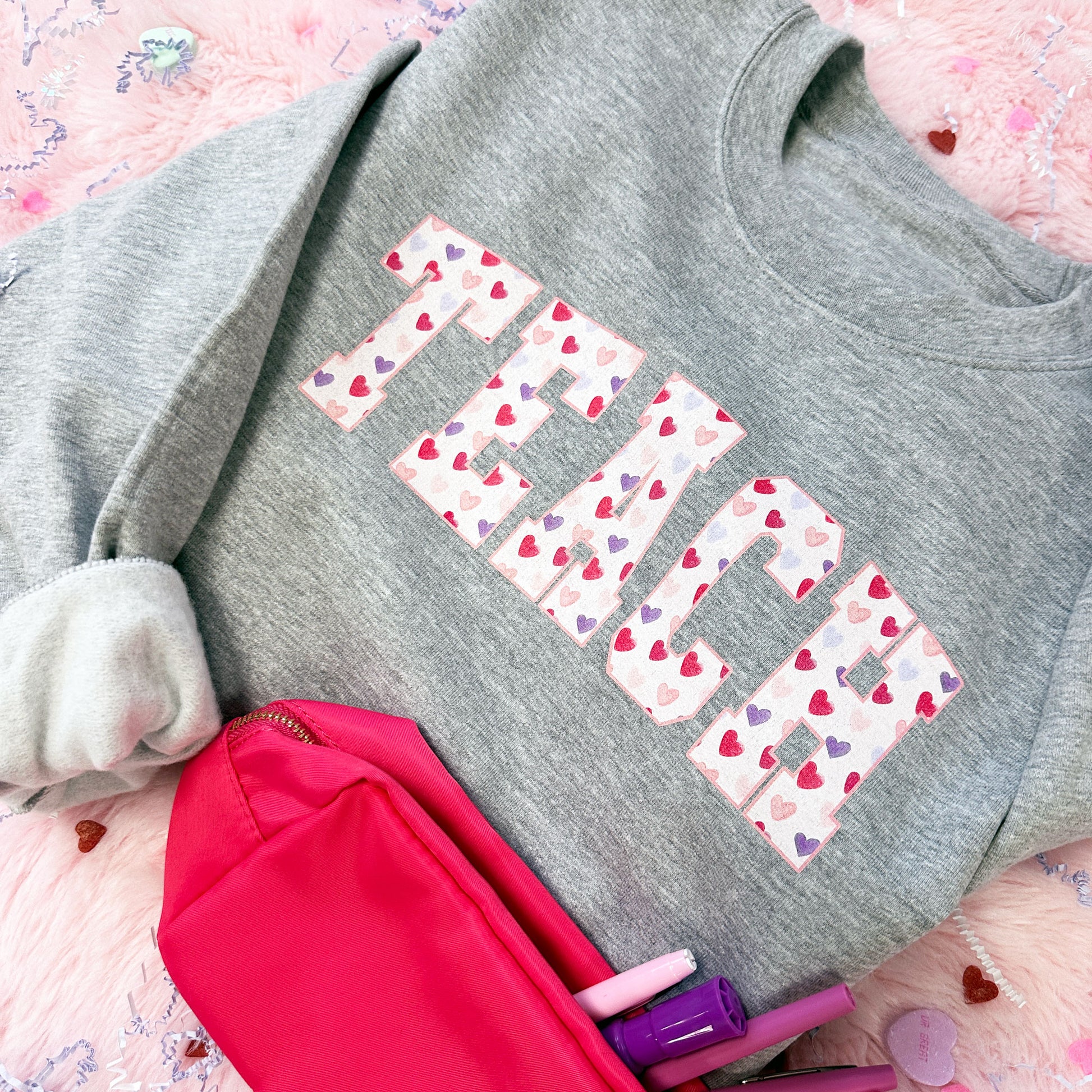 athletic heather crewneck sweatshirt with an athletic block TEACH design featuring a watercolor heart pattern fill.