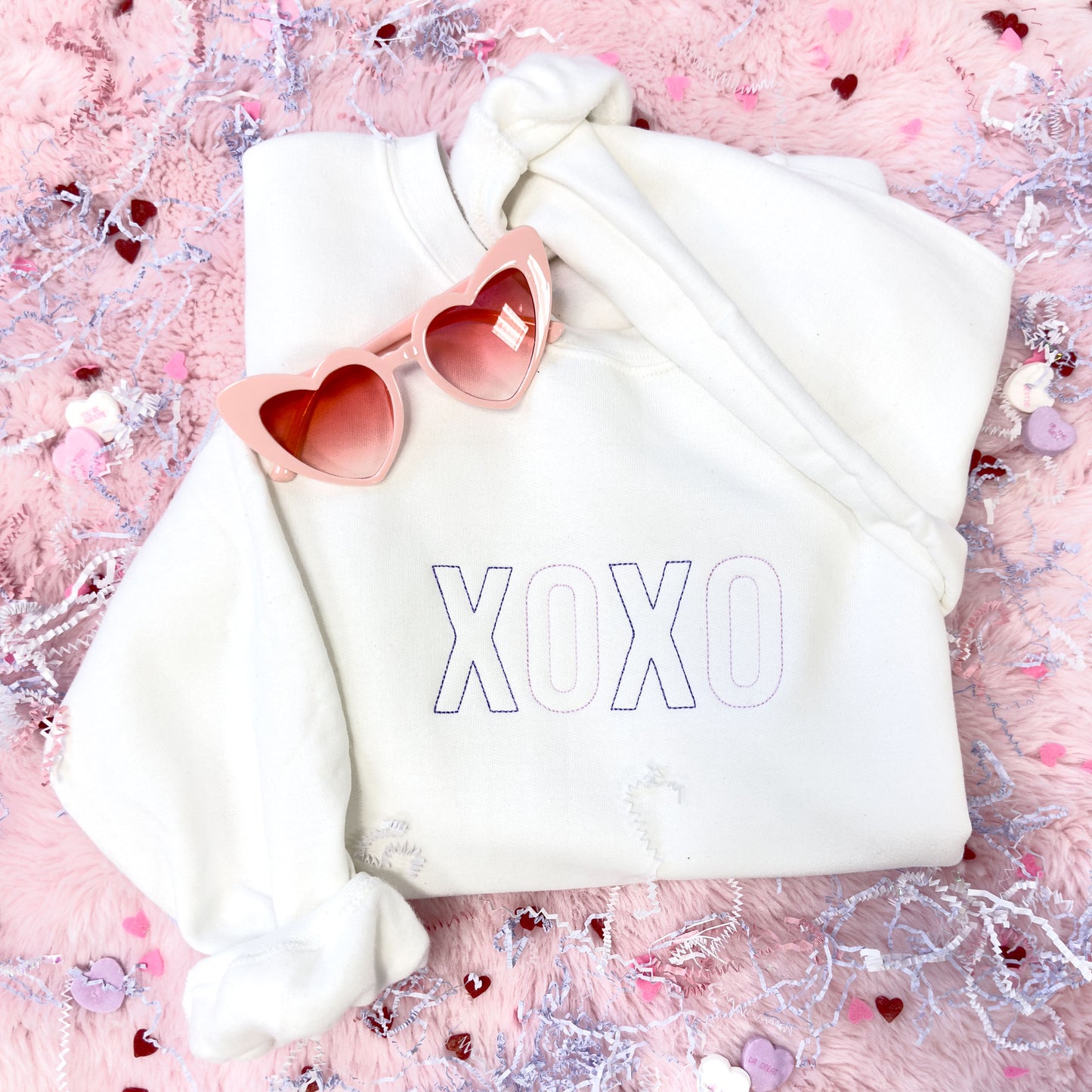 white sweatshirt with XOXO embroidered across the chest in a stitched font