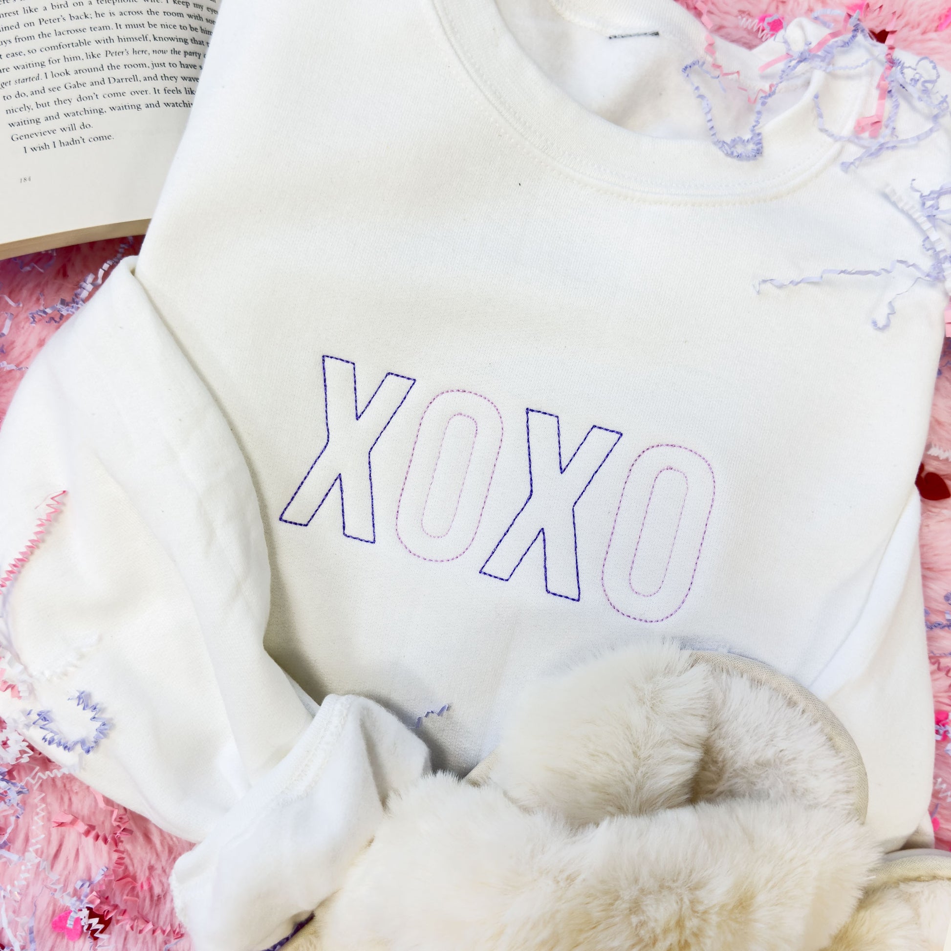cozy crewneck sweatshirt in white with a purple and lilac XOXO embroidered design across the chest