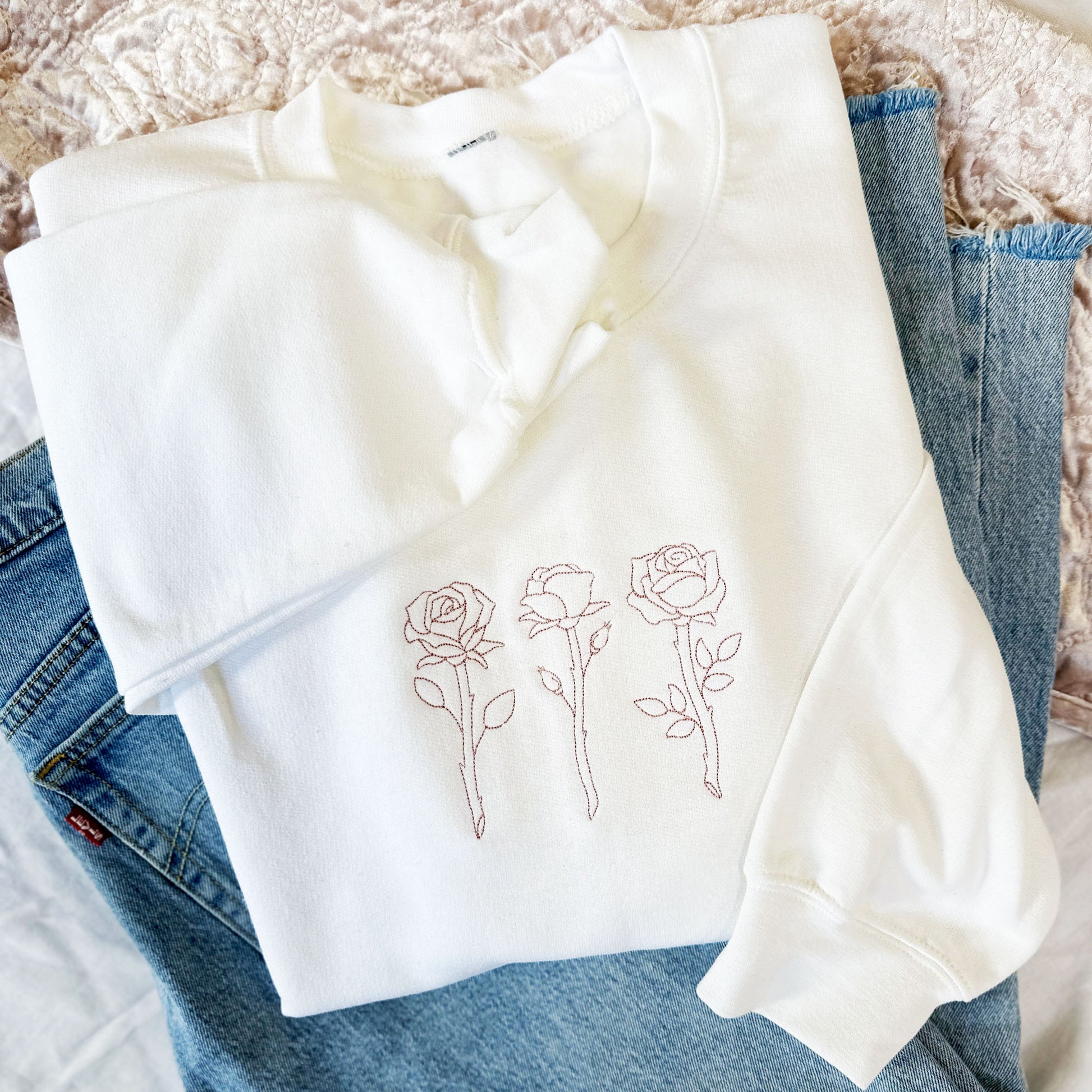 blue jeans paired with a white crewneck with roses embroidered in a pink thread on the center chest