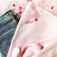 pink crewneck sweatshirt with a custom name embroidered in a script font  along the neckline with mini heart at the end
