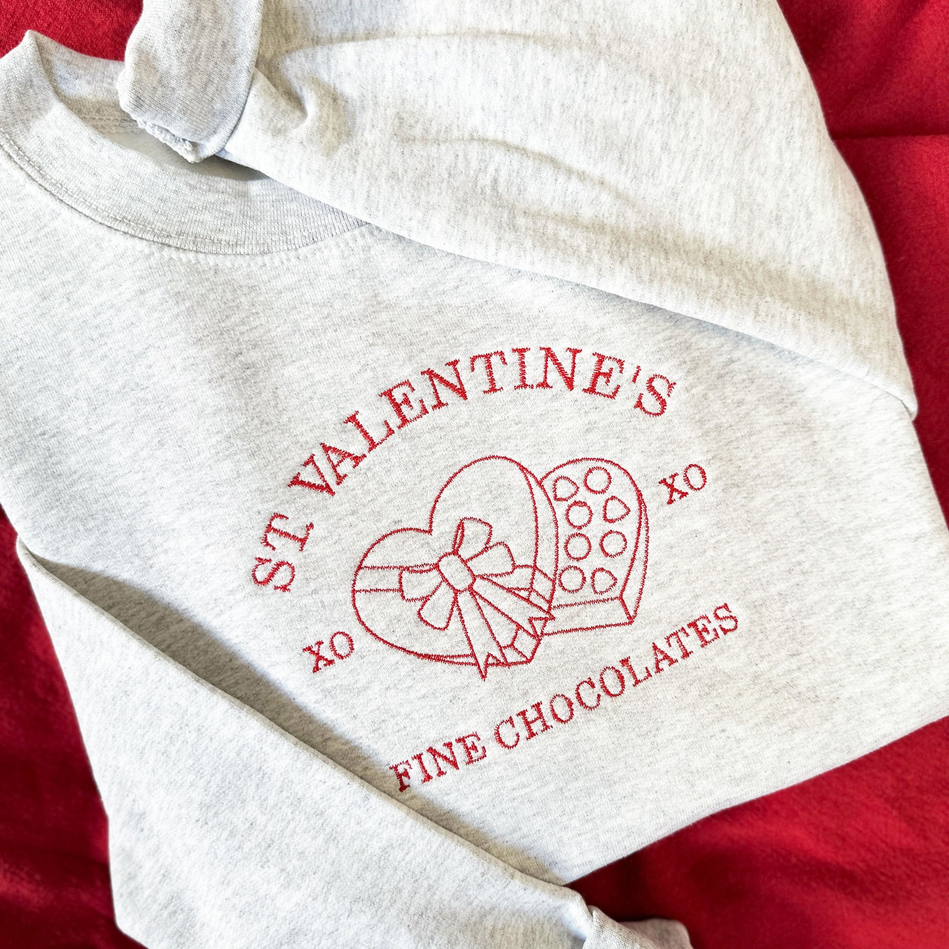 close up of ash gray sweatshirt with a St. Valentine's Fine Chocolates Shop embroidered design on the center chest