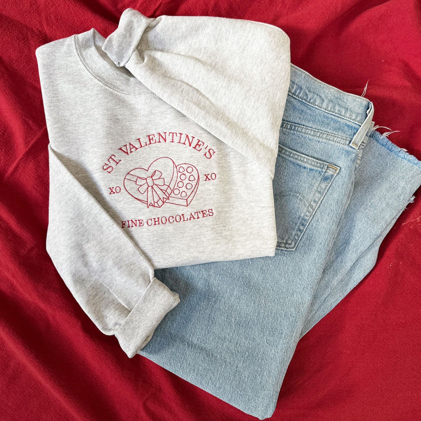 blue jeans paired with a gray crewneck sweatshirt with a red  valentine's chocolate and chocolate heart gift box embroidered on the center chest
