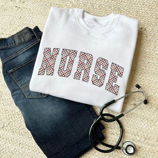outfit flat lay featuring dark blue jeans, stethoscope, and a white crewneck sweatshirt with NURSE printed in a christmas gingham pattern