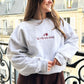 Woman on french balcony modeling la vie en rose with rose design embroidered ash sweatshirt