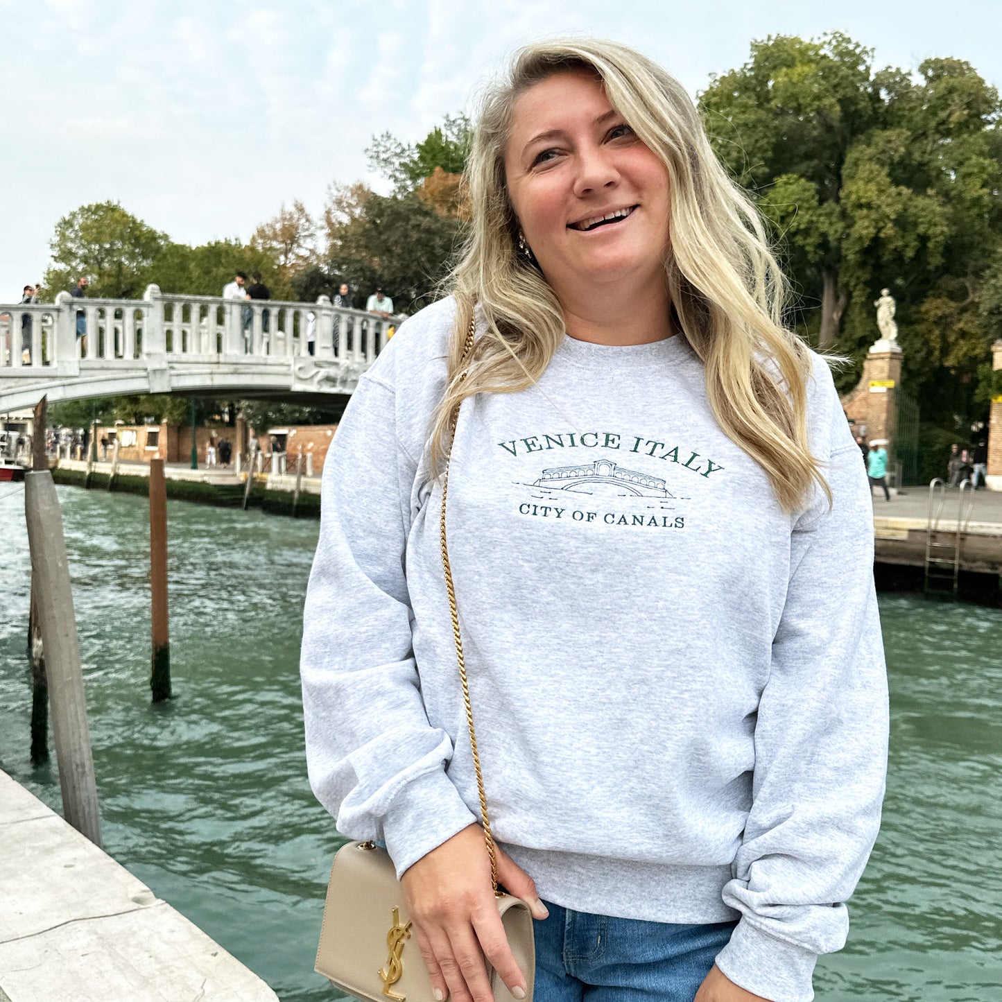 Woman styling an ash crewneck sweatshirt showcasing sketched venice bridge and venice italy city of canals text embroidered in ivy thread