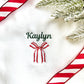 close up image of an embroidered name and festive holiday ribbon bow on a white sweatshirt