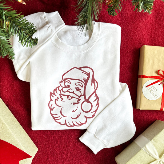 flat lay image of a white santa print sweatshirt surrounded by presents and a christmas tree