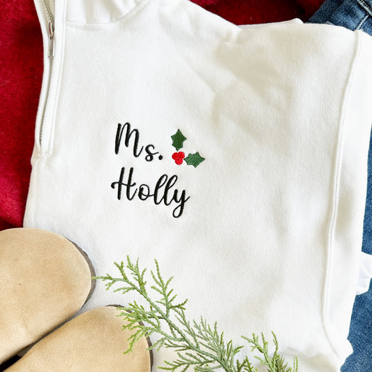 close up image of a custom name and festive holiday design embroidered on a white quarter zip sweatshirt