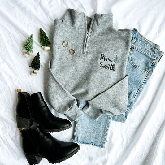 outfit flat lay image featuring an oxford quarter zip with custom name and mini evergreen tree embroidery, gold hoop earrings, blue jeans, and black boots
