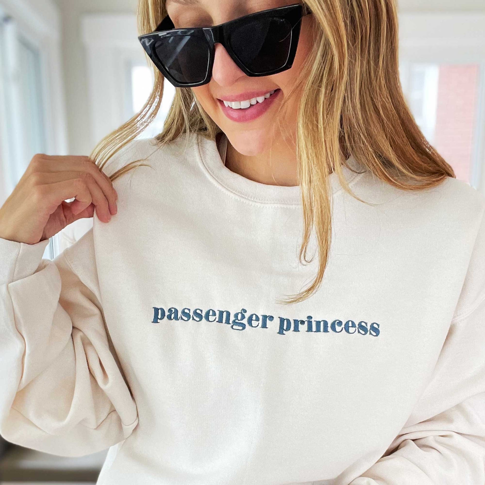 Young woman wearing an embroidered sweet cream crewneck sweatshirt with passenger princess embroidered in french blue thread