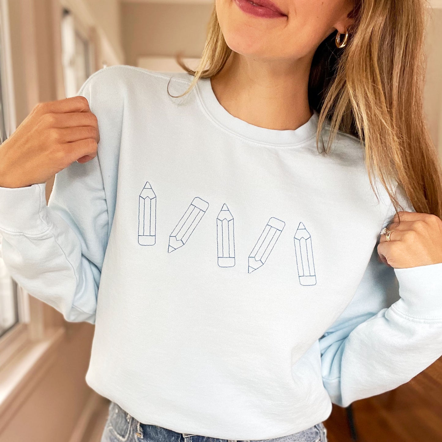 teacher wearing chambray crewneck sweatshirt with cute stitched pencils embroidered across the chest