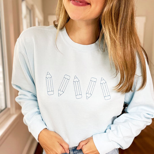 woman wearing a light blue comfort colors crewneck pullover with stitched pencil embroidery design across the chest