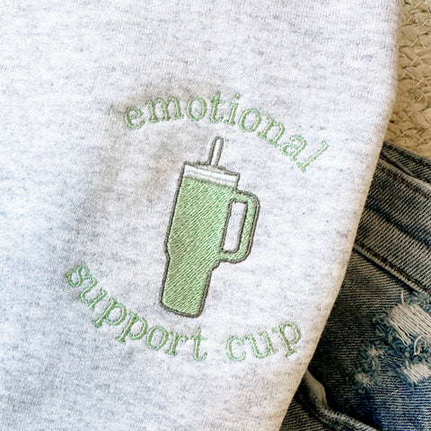 close up of an embroidered sweatshirt with an 'emotional support cup' sage green design