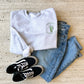 flat lay layout of an outfit featuring vans, jeans, and a crewneck sweatshirt with a stanley cup embroidered design on the left chest.