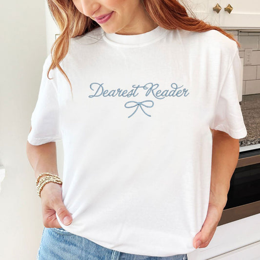woman wearing a white comfort colors t-shirt with embroidered dearest reader with bow Bridgeton design in baby blue thread