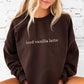 woman wearing an oversized dark chocolate crewneck sweatshirt with embroidered iced vanilla latte across the chest in natural thread and schoolbook lower case font