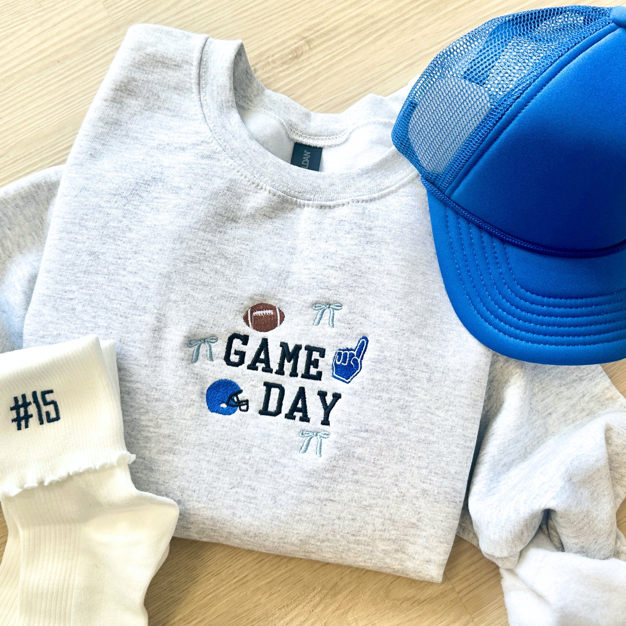 Gray sweatshirt with 'Game Day' design, blue cap, and white socks on a wooden surface