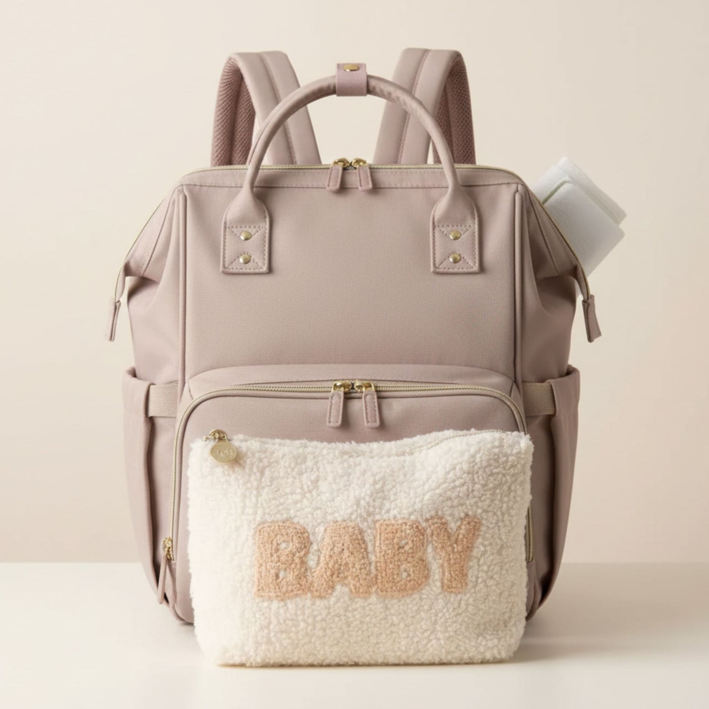 Pink backpack with a fluffy pouch labeled 'BABY' on a light beige background