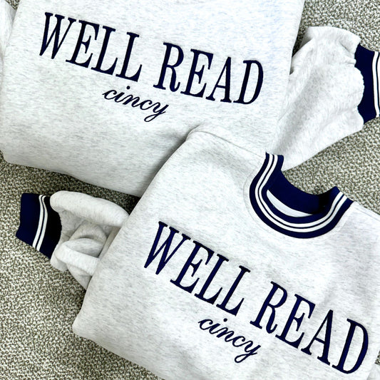 Two white sweatshirts with 'WELL READ cincy' text on a textured surface.