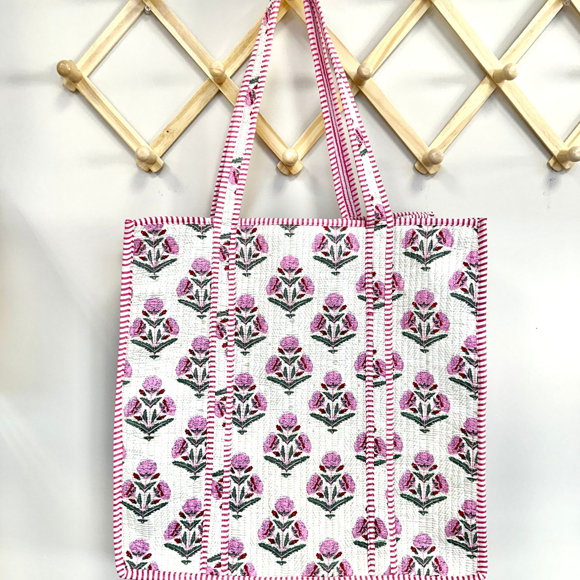 Floral patterned tote bag with pink and white stripes hanging on a wooden rack.