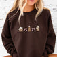 girl wearing a dark chocolate crewneck sweatshirt with custom gingerbread houses and bows embroidered across the chest
