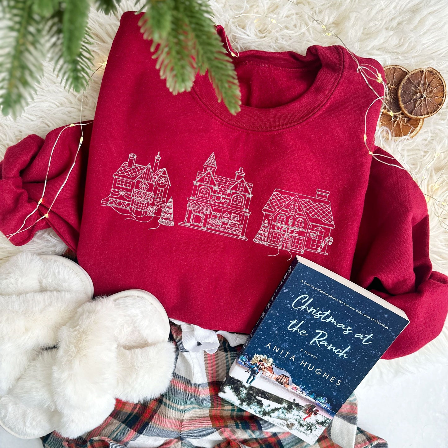 christmas styled flat lay of a cardinal red crewneck sweatshirt with embroidered stitched christmas village in white thread