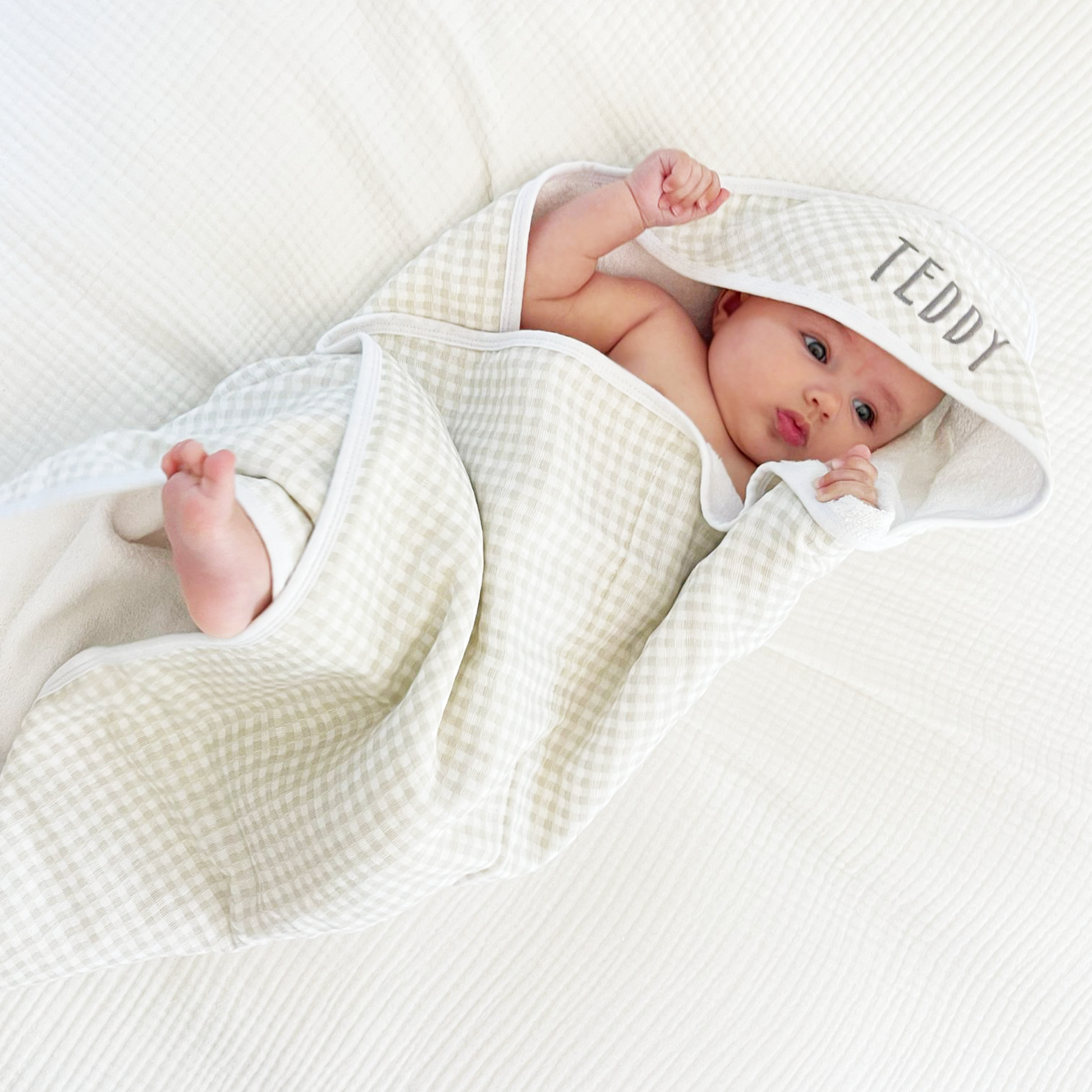 baby wrapped in a tan plaid hooded bath towel with name embroidered on the hood in a dark gray thread