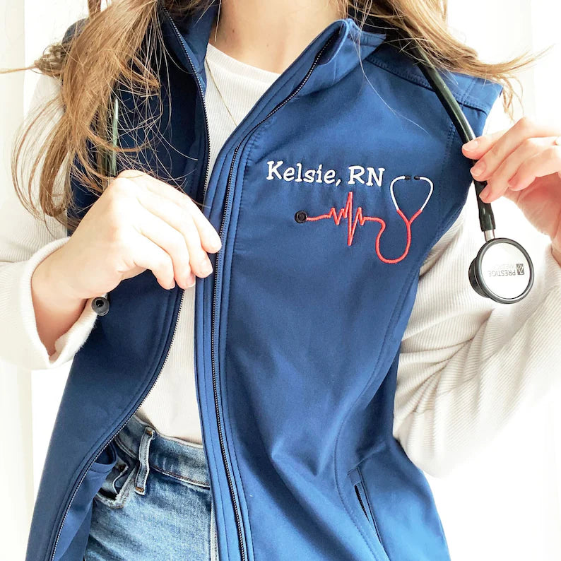 young woman wearing a blue soft shell vest with embroidered nurse stethoscope and name on the left chest