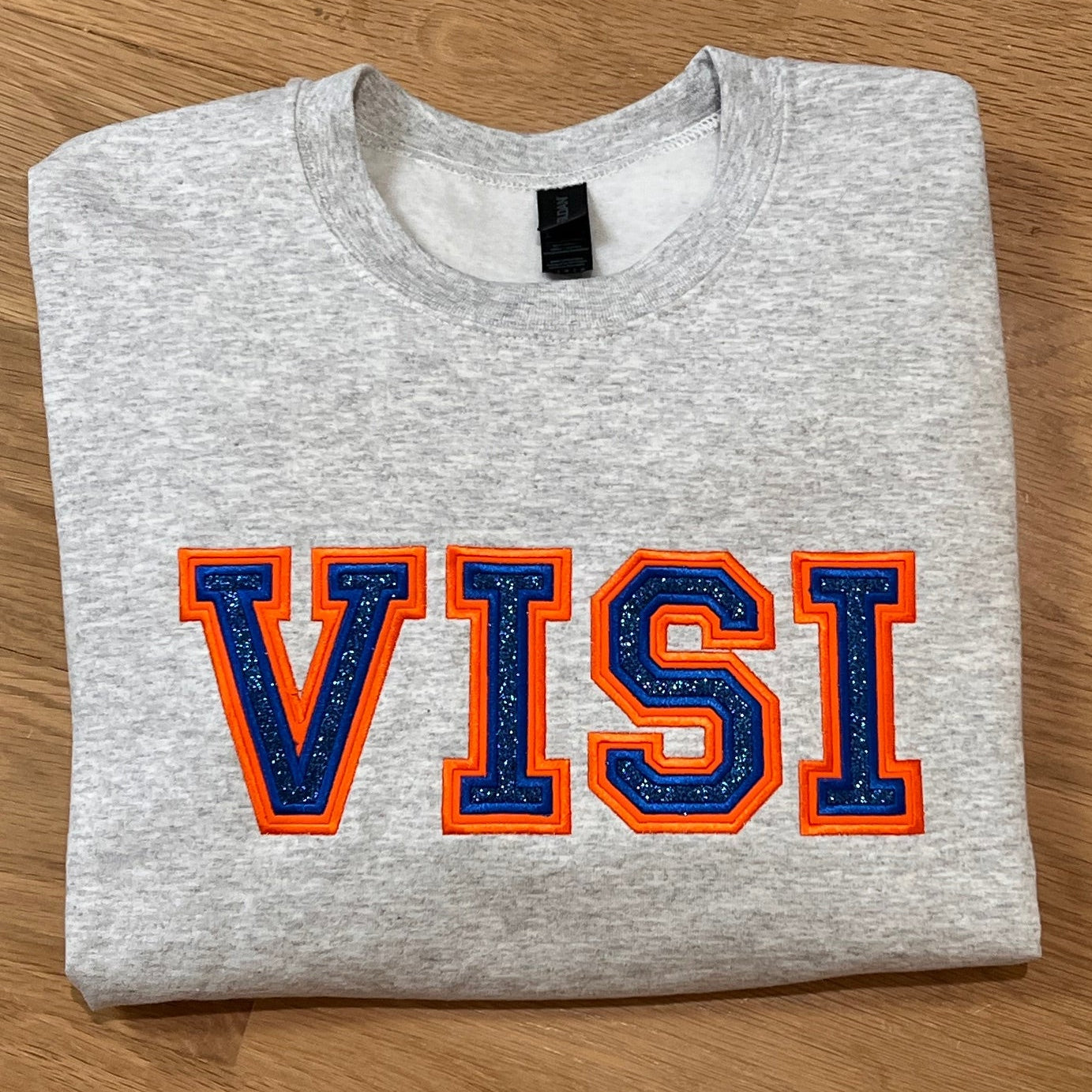 Gray tsweatshirt with orange and blue 'VISI' design on a wooden surface