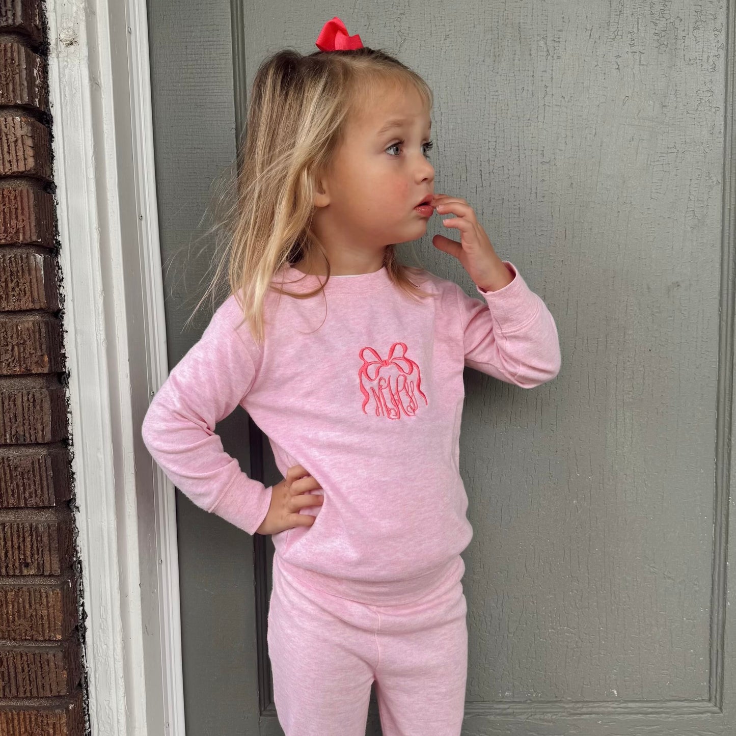 little girl wearing a pink long sleeve flare jogger set with an embroidered bow monogram on the center chest