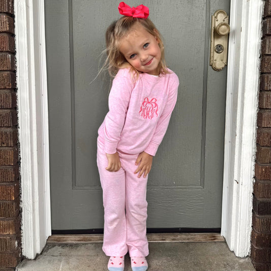 little girl wearing a pink long sleeve flare jogger set with an embroidered bow monogram on the center chest