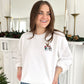Woman wearing a white sweatshirt with Christmas-themed designs in a festive setting.