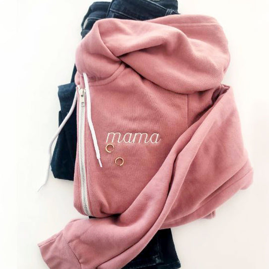 mauve bella and canvas full zip hooded jacket folded on top of a pair of jeans featuring a personalized embroidery reading mama in a small script font on the left chest