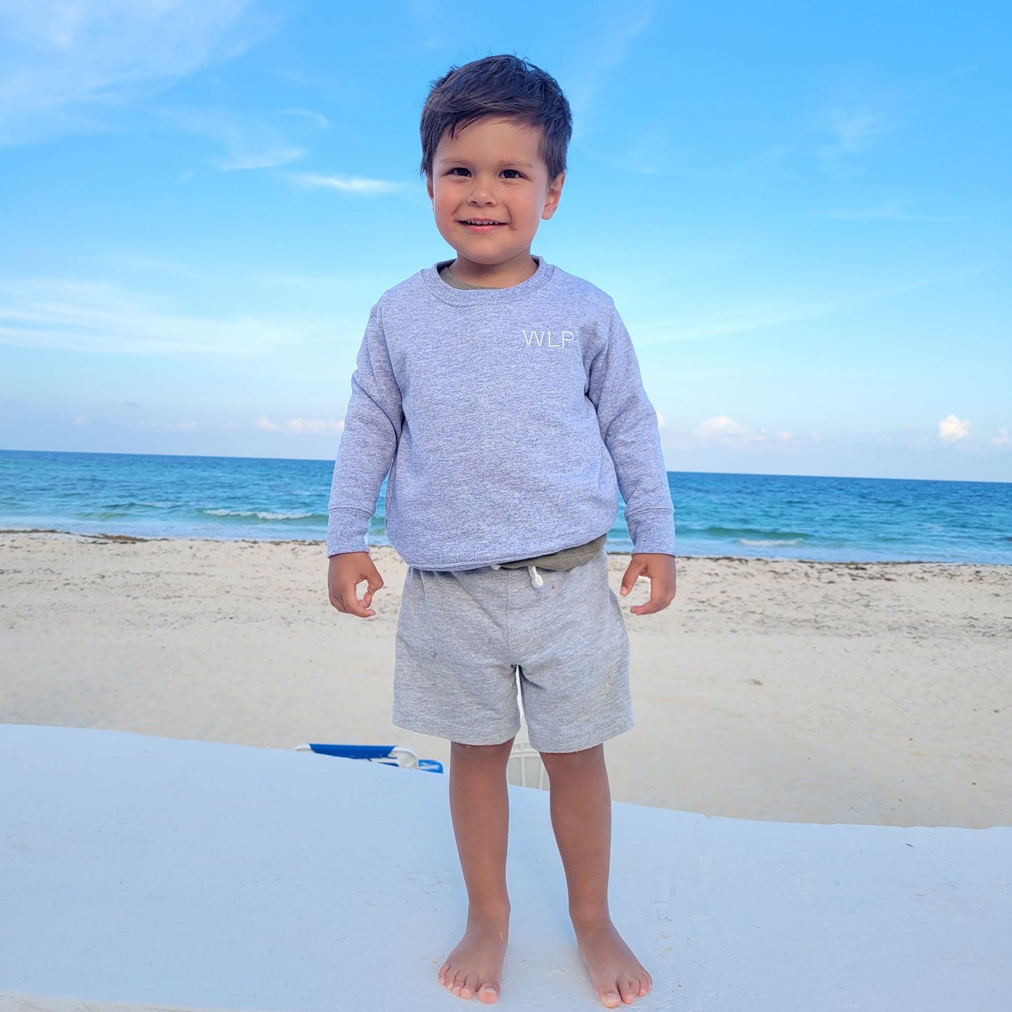 little boy at the beach wearing crewneck with initials on left chest
