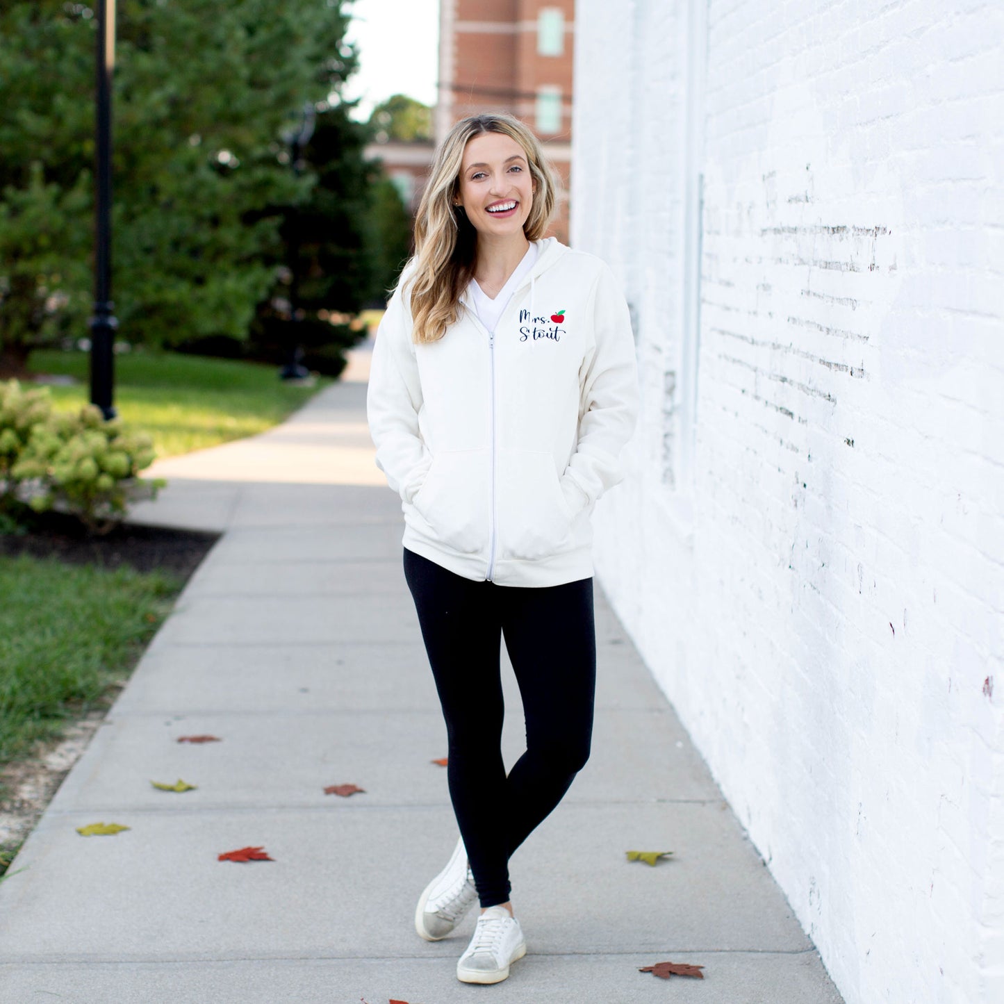 Woman walking down sidewalk wearing a hooded fleece jacket with a custom name and small apple embroidery in black and red thread