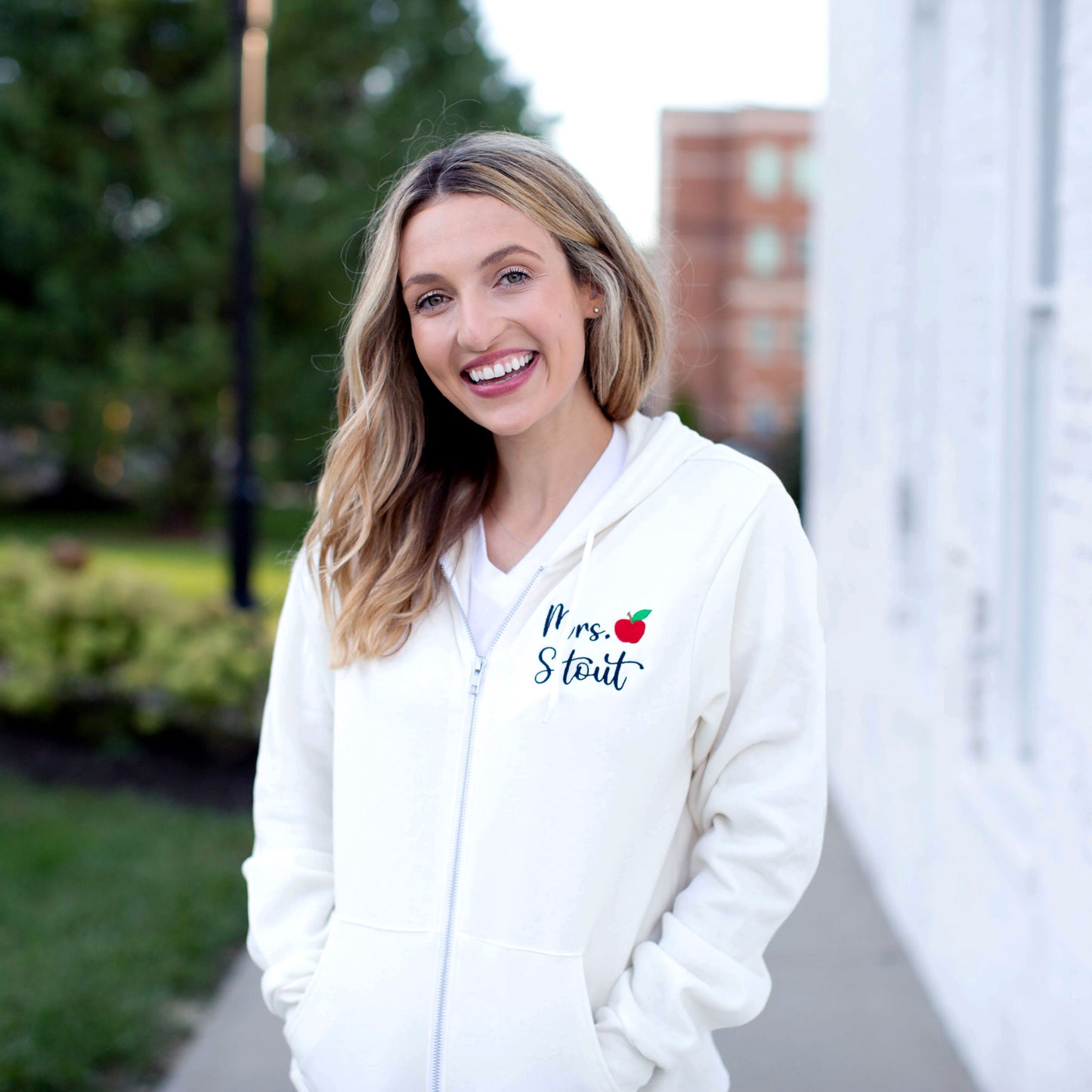 woman wearing a white jacket with a teacher name and small red apple embroidered on the left side