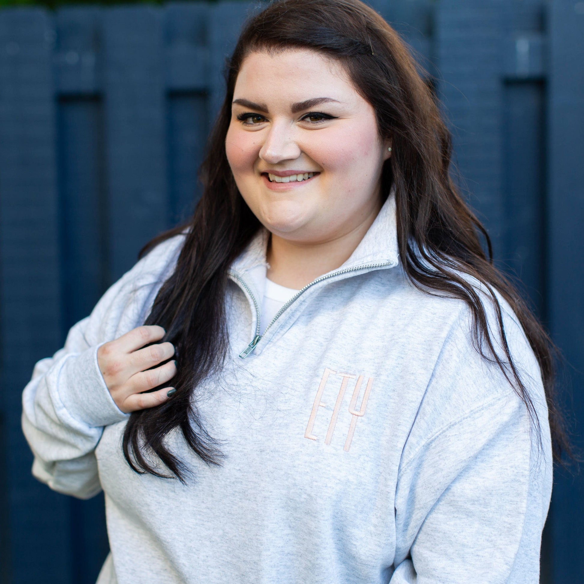 woman wearing a gray pullover quarter zip sweatshirt with a custom three letter embroidered monogram