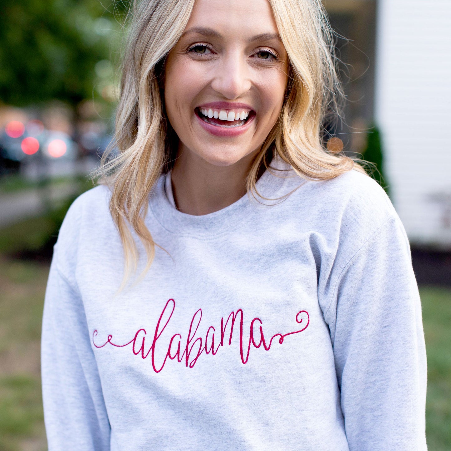 woman wearing ash crewneck sweatshirt with a custom state name embroidered across the center in red thread
