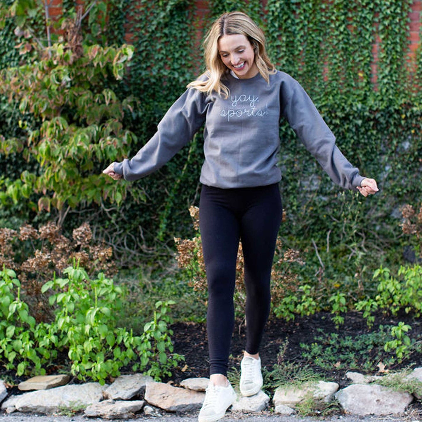 woman wearing a crewneck pullover sweatshirt in a dark gray with custom embroidery reading yay, sports in white thread, large across the chest