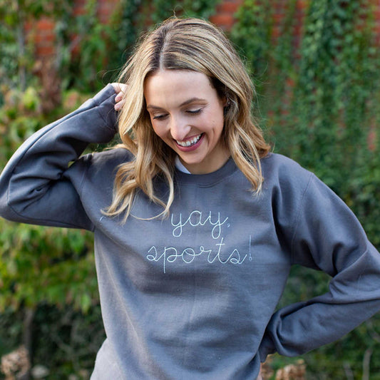 young woman laughing and wearing a charcoal gray crewneck pullover with yay sports! stitched in white thread across the chest
