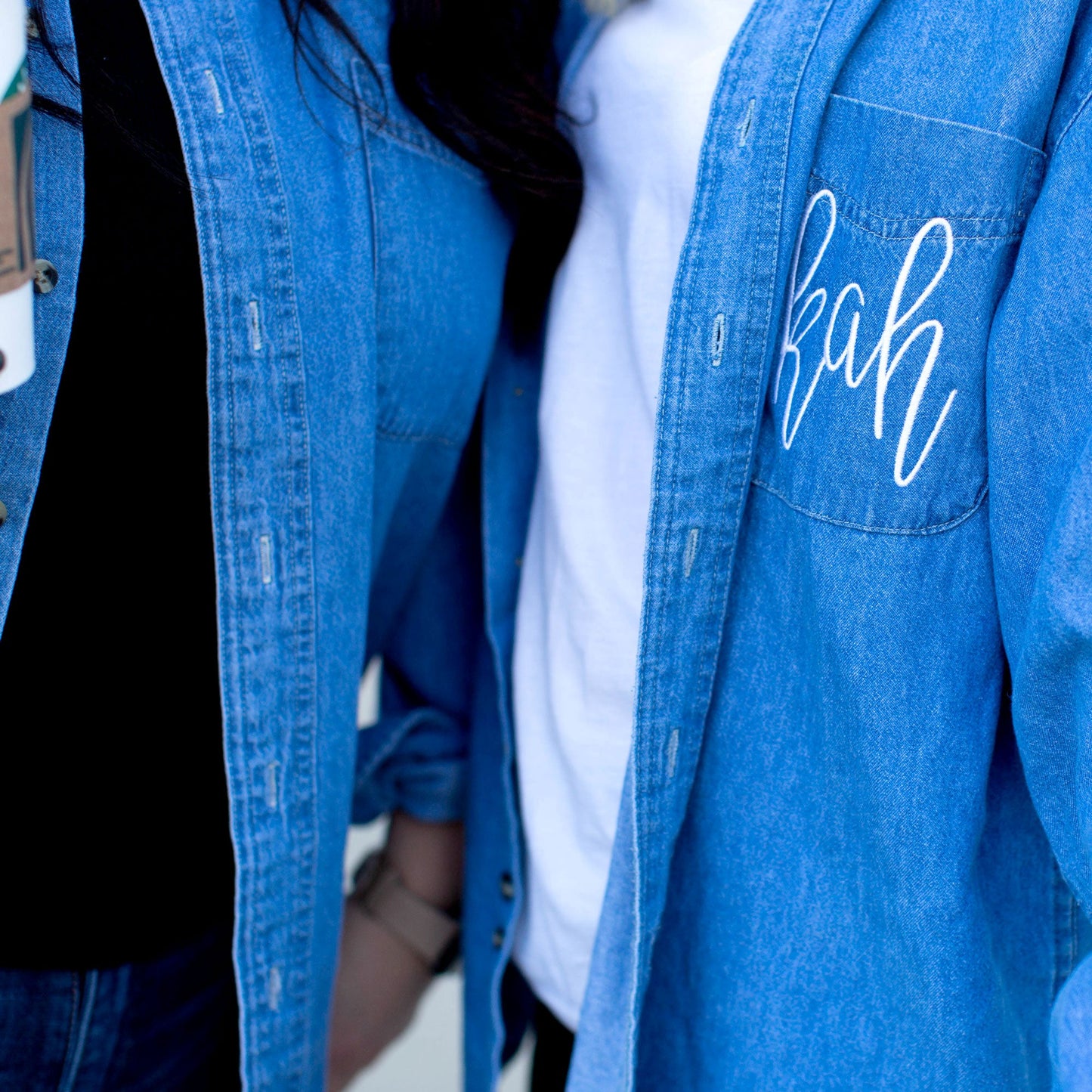 close up of white script monogram embroidery on pocket of a denim button up shirt