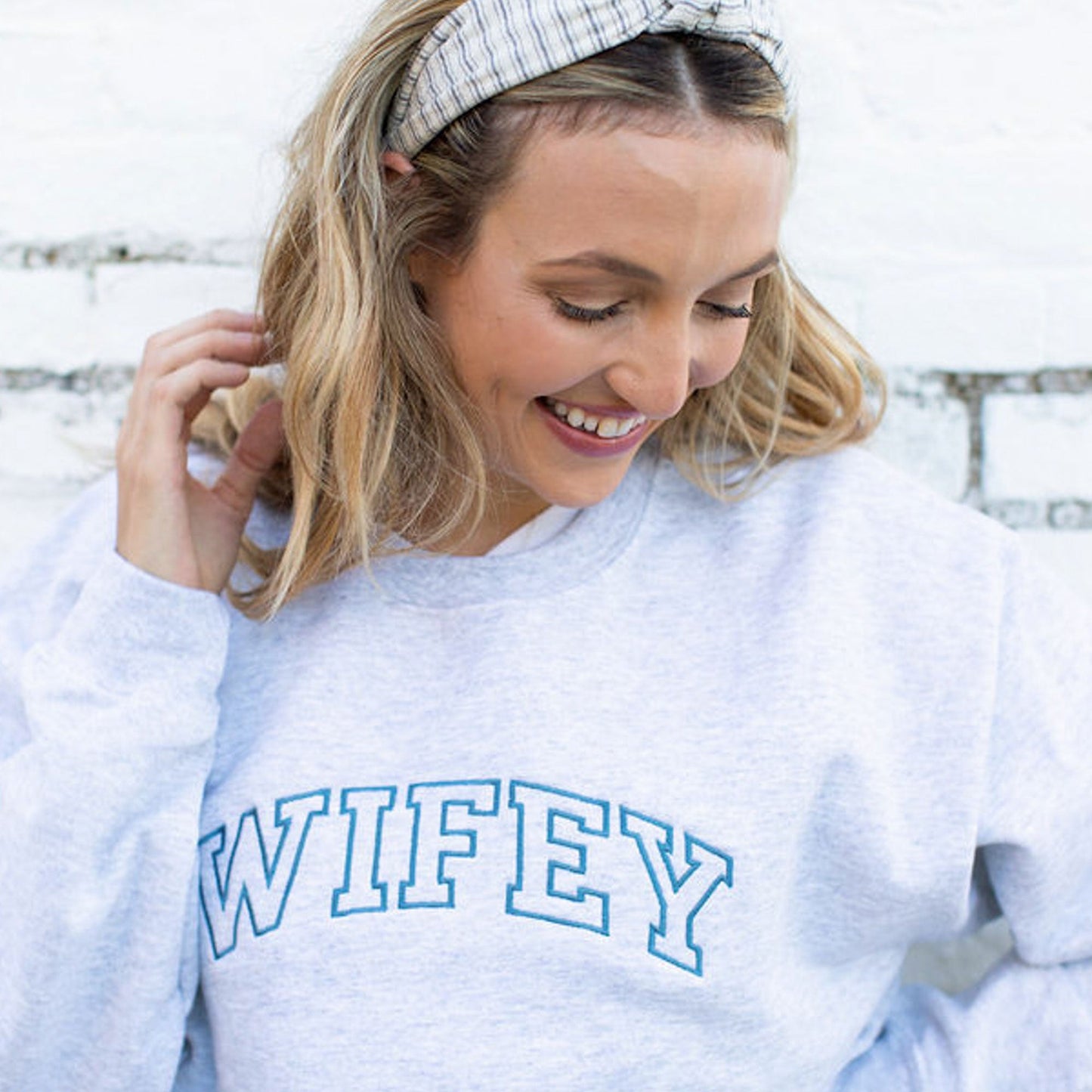 woman smiling and wearing a sweatshirt with wifey embroidered in french blue thread across the chest