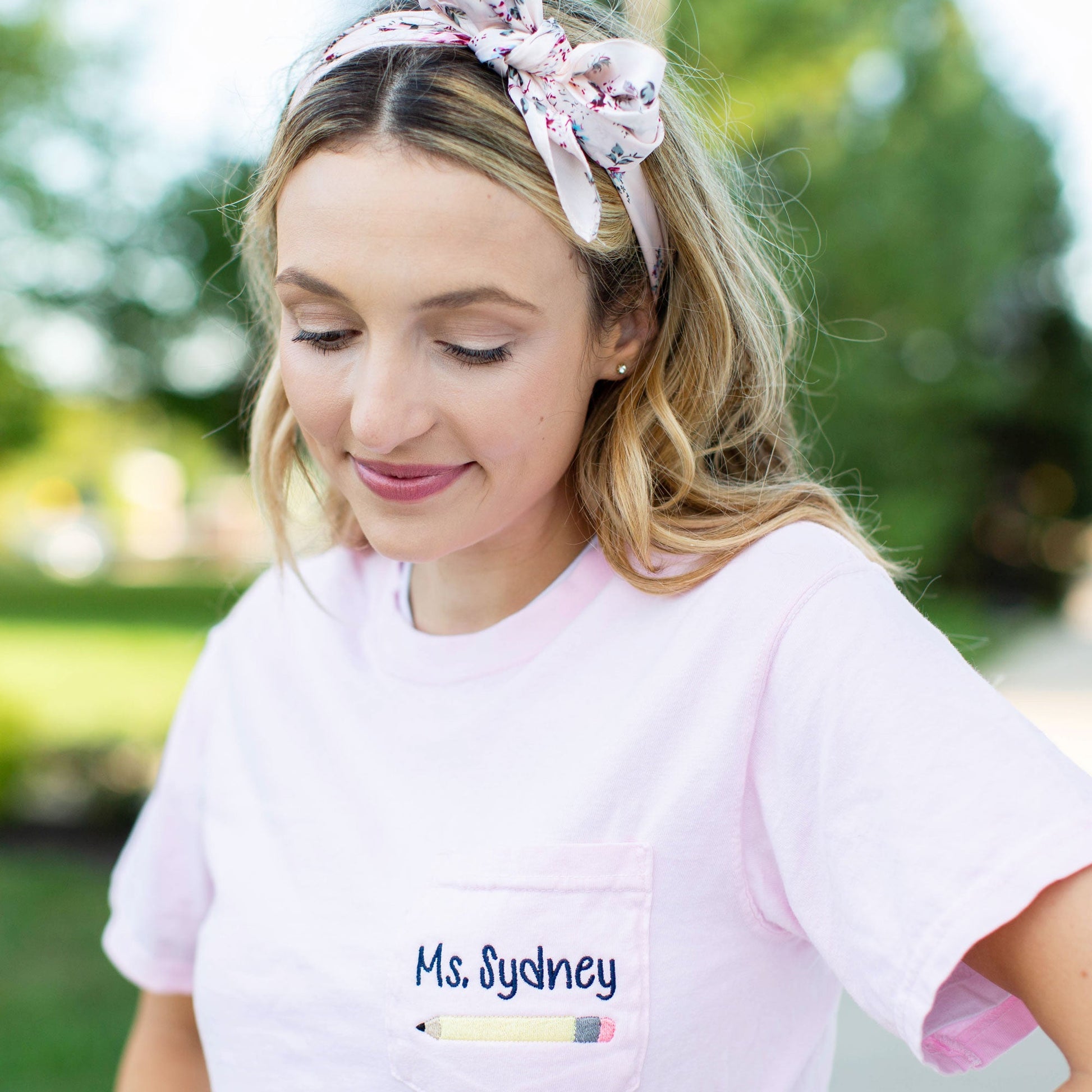 Blonde woman wearing short sleeved pocket tee with teacher name and pencil embroidered on pocket 