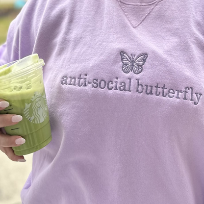 girl wearing a lavender sweatshirt with a mini purple butterfly embroidered above the words anti-social butterfly on the chest